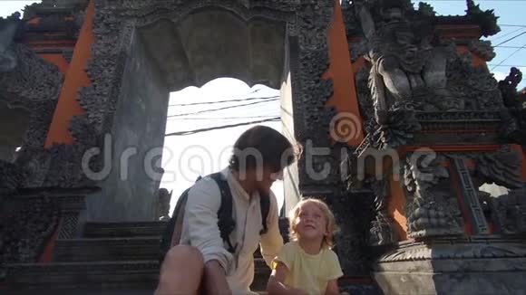 一对父子游客坐在巴厘岛寺庙的楼梯上在一个动作上自拍的慢镜头视频的预览图