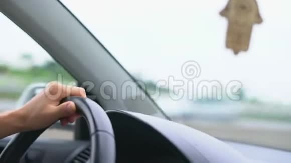 司机在仪表板和挡风玻璃背景下的方向盘上的手视频的预览图