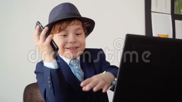 男孩商人手里拿着电话坐在办公室里微笑着在笔记本电脑附近工作视频的预览图