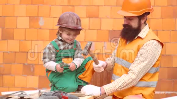 父子一起盖房子童年概念带着橙色头盔或头盔的幼儿帮助他蓄胡须视频的预览图