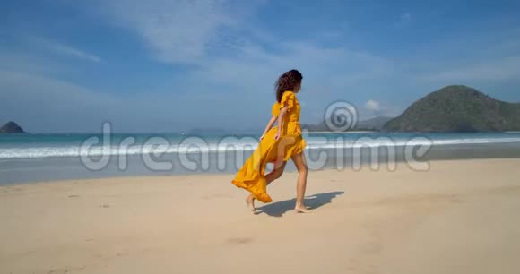 年轻快乐的黑发女郎穿着黄色的裙子沿着沙滩奔跑呼吸新鲜空气欣赏着令人叹为观止的海景视频的预览图