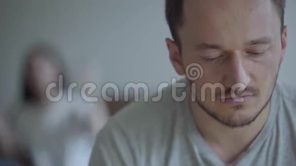 特写镜头前哭着的男人和他在后台坐在沙发上的愤怒的妻子的画像视频的预览图