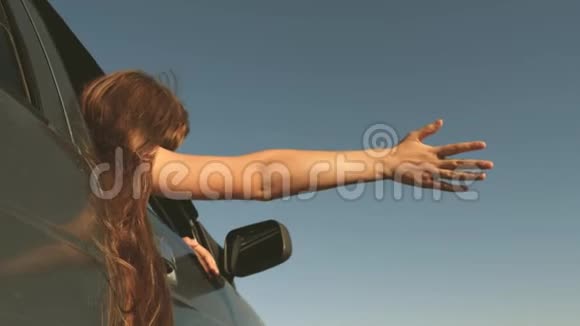 快乐的女旅行者在乡间小路上开车从车窗伸出的手抓住了风长发女孩是视频的预览图