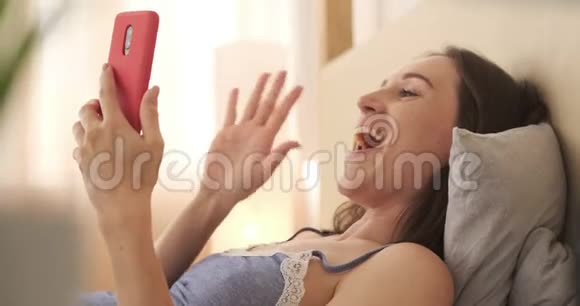兴奋的妇女在床上用手机聊天的视频视频的预览图