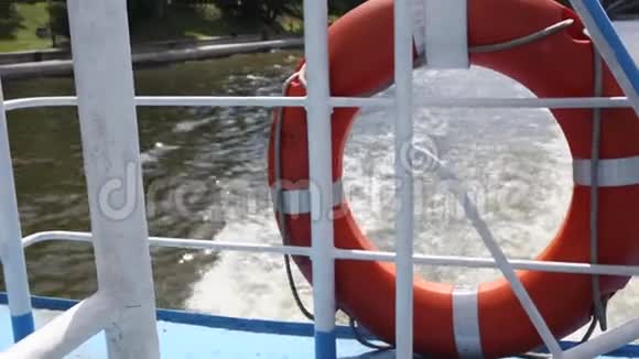 阳光明媚的日子橙色救生圈挂在船栏杆上背景中的水波船的船尾景色视频的预览图