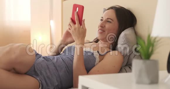 穿着睡衣在手机上享受媒体内容的轻松女人视频的预览图