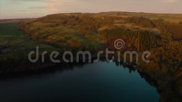 英国金色日落时平静的湖面和高大的树木的空中镜头视频的预览图
