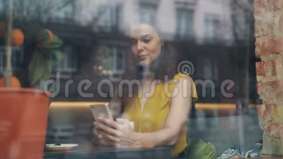 可爱的女学生在舒适的咖啡馆里喝咖啡和使用智能手机视频的预览图