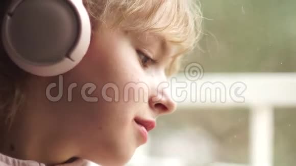 用粉色无线耳机近距离拍摄一个美丽悲伤的少年女孩的肖像青少年和音乐视频的预览图