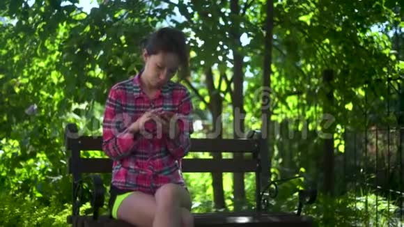 快乐女学生坐在城市公园的长凳上用智能手机年轻女子微笑着用应用程序长时间视频的预览图