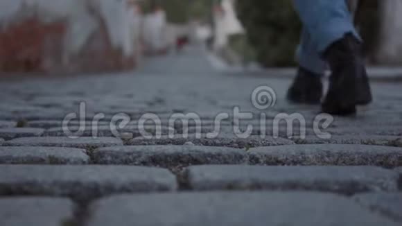 一个穿着黑色靴子和牛仔裤的女人在欧洲城市的鹅卵石街道上走得很近视频的预览图