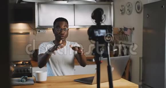 快乐的年轻黑人受欢迎的社交媒体博主男子为他的在线博客使用相机在家慢镜头直播视频的预览图