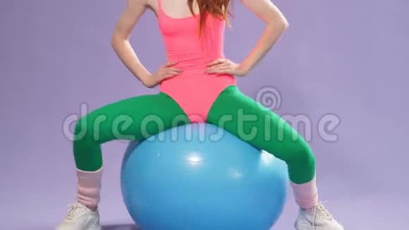 女士在家接受健身训练双手分开双手放在腰部和腿部坐在健身球上视频的预览图