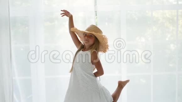 穿着连衣裙和草帽的女孩正在一扇大窗户的背景上旋转视频的预览图