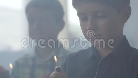 两个弟弟在黑暗的烟雾弥漫的房间里玩火一个男孩在背景中点燃了打火机另一个男孩点燃了视频的预览图
