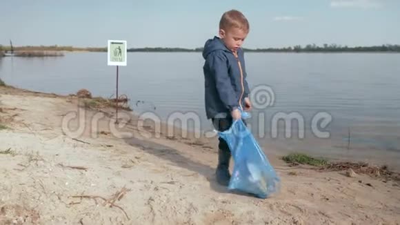 停止污染可爱的男孩在清理了塑料垃圾和垃圾后在河滩的指向标志上拉了一大袋垃圾视频的预览图