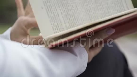 侧视女性手与漂亮的指甲保持书在红色封面白种人女人坐在户外看书视频的预览图