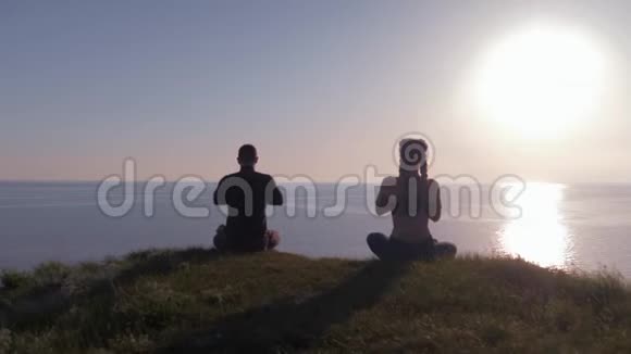 瑜伽锻炼日落时在陆地上运动的情侣坐在山顶的莲花位置看海观海视频的预览图