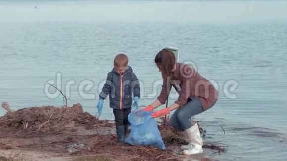 生态保育妈妈和小男孩志愿者清洁污染的自然从塑料垃圾附近的水河滨视频的预览图