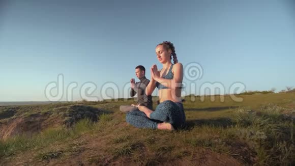 瑜伽的生活方式运动的女人和男人一起在草地上冥想在天空的背景下坐在莲花的位置视频的预览图