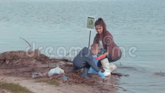 家庭清洁海滩年轻的女志愿者带着小男孩清洁污染的自然从塑料垃圾附近的水视频的预览图
