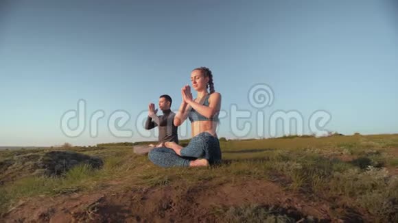 瑜伽宗教运动双人在天空的背景下在草地上一起冥想视频的预览图