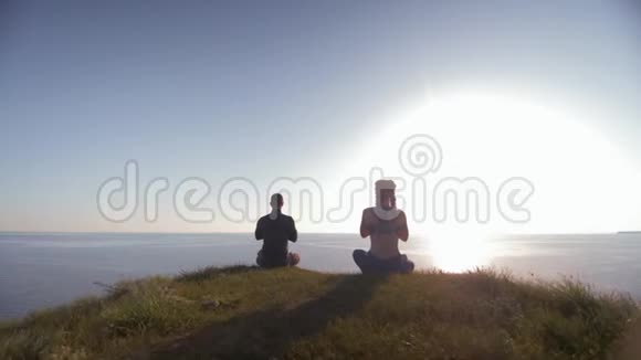 瑜伽在平静的大海背景下男人和女人坐在山顶上沉思日落视频的预览图