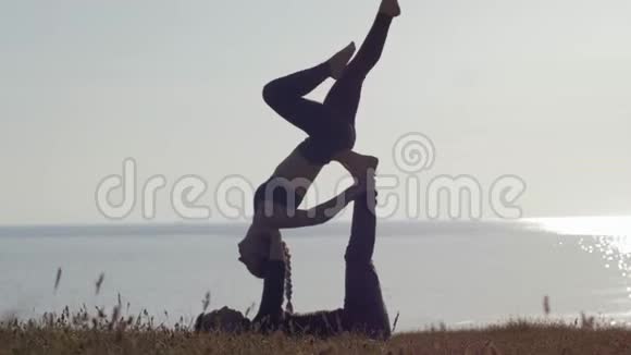 在大自然的背景下锻炼身体运动情侣在海和日落的背景下在草地上练习杂技瑜伽视频的预览图