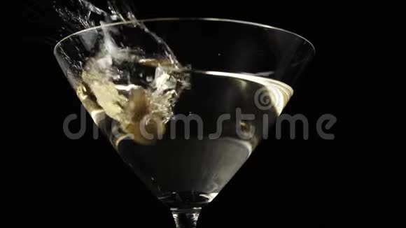 豪华马提尼两颗美味的绿橄榄用马提尼在黑色背景下倒入玻璃杯中视频的预览图