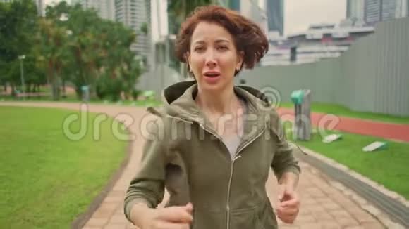 在户外运动慢动作慢动作慢动作年轻有魅力穿着帽衫的女人在绿色城市公园跑步视频的预览图