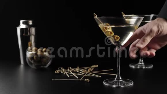豪华马提尼手拿着一杯摆在前景上的甜马提尼摆着橄榄和鸡尾酒棒的桌子视频的预览图