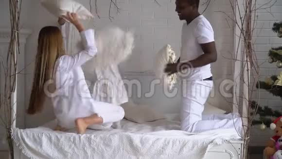 快乐混血家庭妈妈非洲爸爸和小女儿在床上玩枕头大战多民族青年视频的预览图