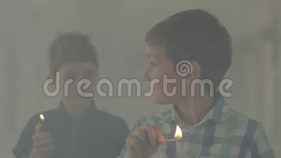 两个弟弟在黑暗的烟雾弥漫的房间里玩火一个男孩在背景中点燃了打火机另一个男孩点燃了视频的预览图