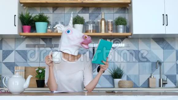 奇怪的搞笑视频戴着独角兽面具的女人在厨房喝咖啡看书视频的预览图