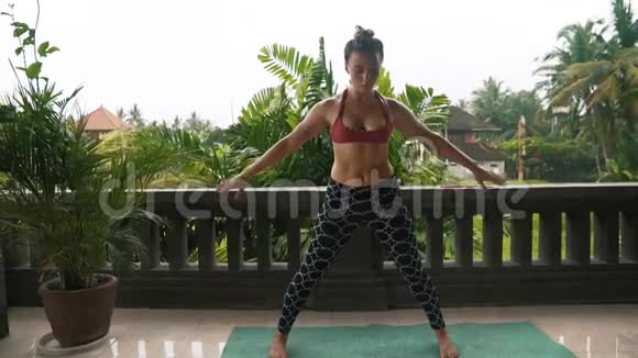 女人在阳台上做瑜伽练习背景是绿色植物视频的预览图