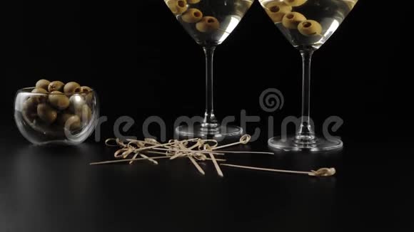豪华马提尼黑桌上装饰着橄榄木棍和两杯马提尼里面有橄榄摄像机移动视频的预览图