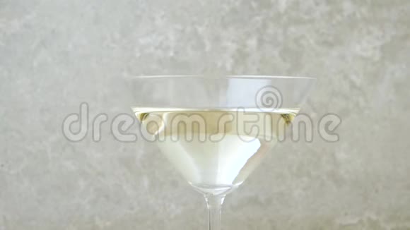 豪华马提尼三个美味的绿色橄榄在鸡尾酒绿色橄榄被扔进玻璃中杯中的马提尼放在浅色背景下视频的预览图