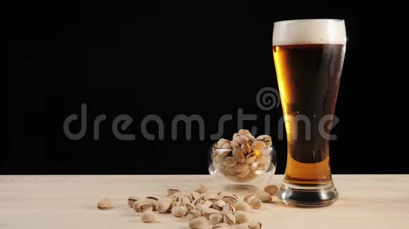 新鲜啤酒在黑色背景下手工从靠近开心果碟的木桌上拿出一杯美味的手工啤酒视频的预览图