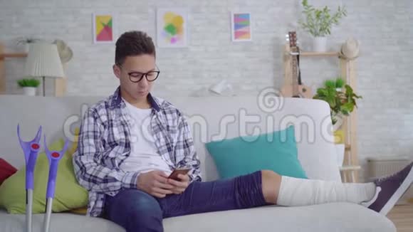 带着绷带的腿断了的亚洲年轻人用智能手机看相机竖起大拇指视频的预览图
