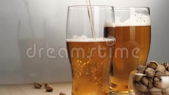 新鲜啤酒在白色背景的木桌上用手将美味的冰镇啤酒和一些开心果倒入啤酒杯碟中视频的预览图