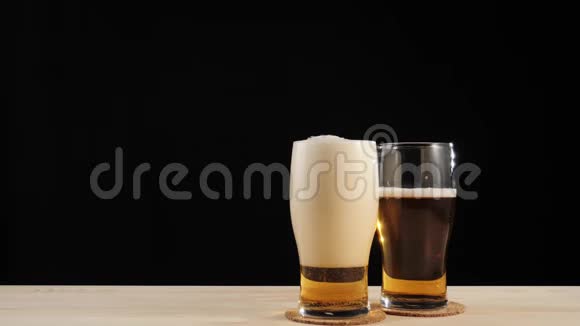 新鲜啤酒啤酒杯上的美味工艺啤酒靠近其他玻璃的杯垫放入黑色背景的木桌中视频的预览图