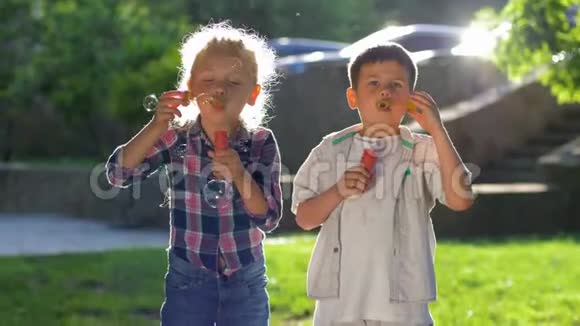 两个小男孩和女孩在户外玩耍并在背光下吹肥皂泡视频的预览图