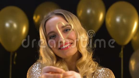 漂亮的金发女人把心形的孟加拉灯对着镜头庆祝视频的预览图