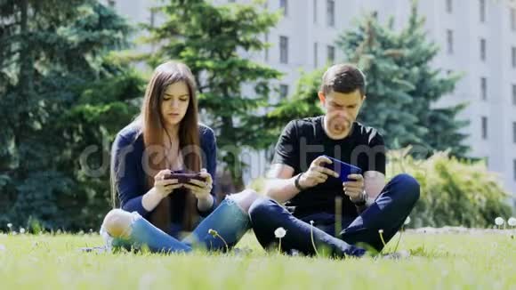 幸福夫妇在智能手机上玩手机游戏坐在公园的草地上男人赢了比赛女人输了视频的预览图