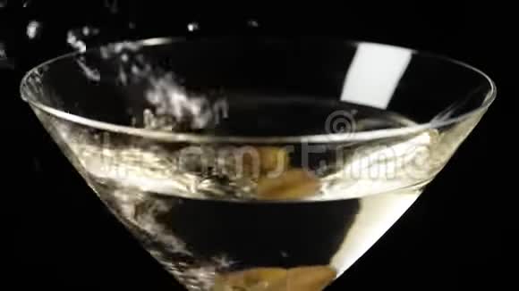 豪华马提尼两颗美味的绿橄榄用马提尼在黑色背景下倒入玻璃杯中佛蒙特州视频的预览图