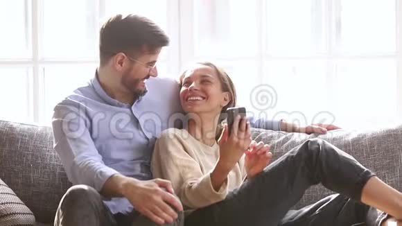 幸福夫妇谈笑风生看着智能手机坐在沙发上视频的预览图