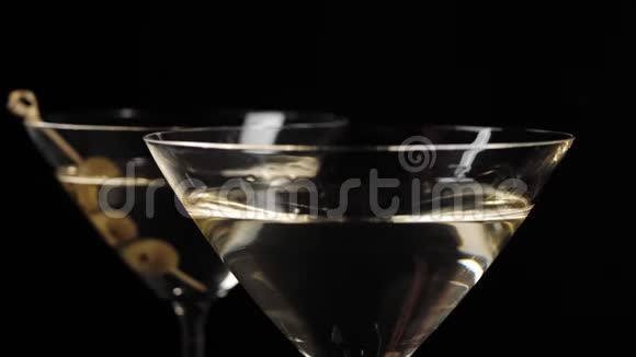 豪华马提尼手把三个美味的橄榄放在鸡尾酒棒上放进杯子里黑桌上放着甜马提尼视频的预览图