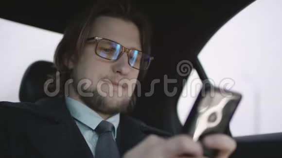 一个英俊的男人棕色头发穿着开心果衬衫穿着灰色外套骑着车通过手机输入信息视频的预览图