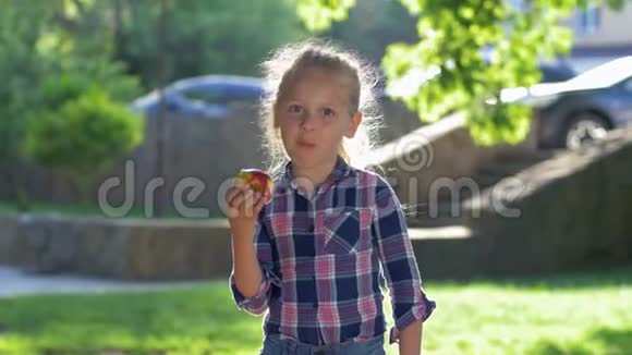 健康的食物快乐的金发女孩的肖像穿着格子衬衫在户外阳光下嚼着一个多汁的苹果视频的预览图