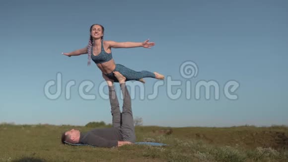 一对夫妇在草地上做杂技表演身穿运动服的年轻白种人正在平衡她的男伴的腿视频的预览图